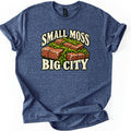 Small Moss Big City Comfort Colors T-shirt in Heather Navy, laid flat. A cluster of red bricks overgrown with green moss sits between the words SMALL MOSS and BIG CITY in cream letters. The shirt has rolled sleeves and lies on a white background.