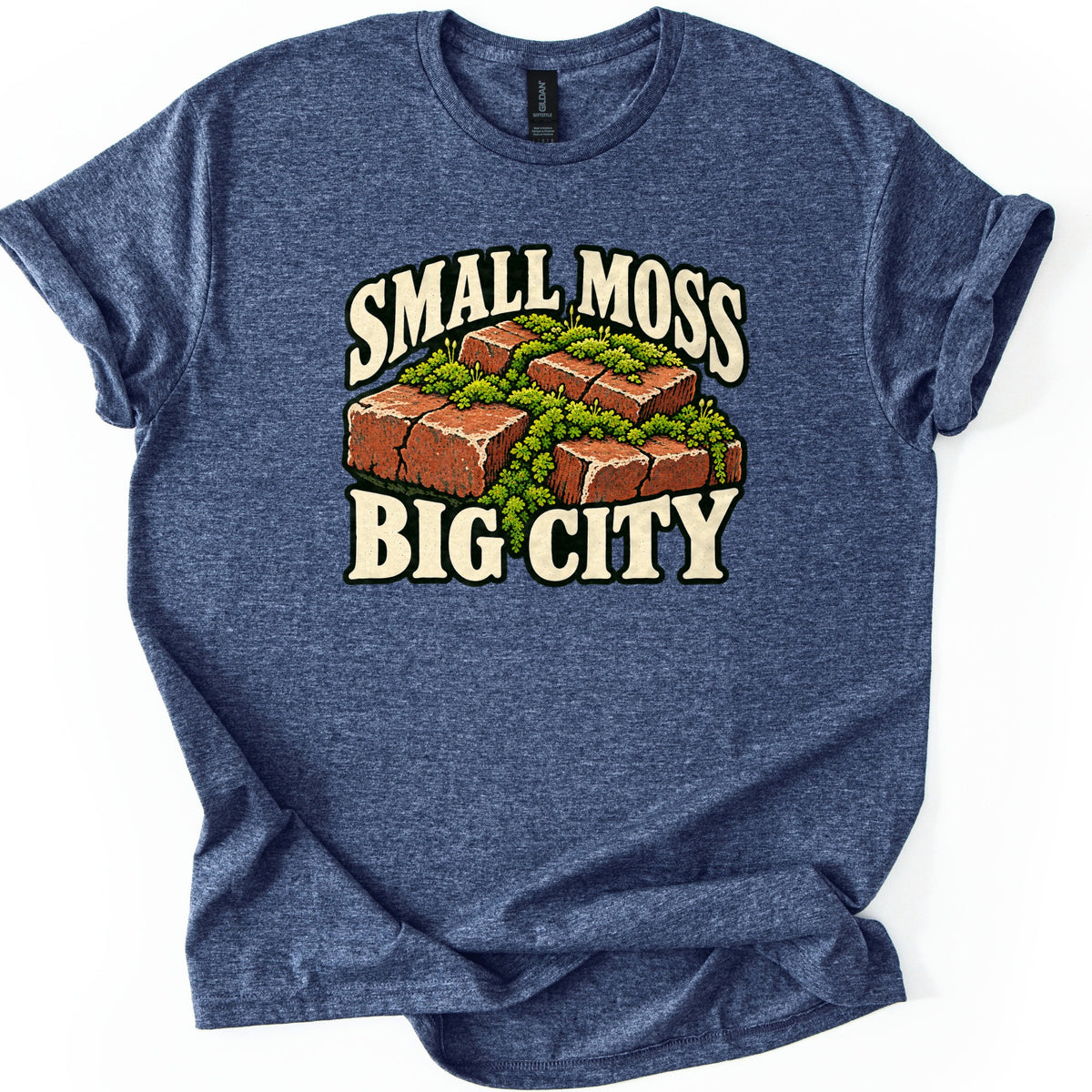 Small Moss Big City Comfort Colors T-shirt in Heather Navy, laid flat. A cluster of red bricks overgrown with green moss sits between the words SMALL MOSS and BIG CITY in cream letters. The shirt has rolled sleeves and lies on a white background.