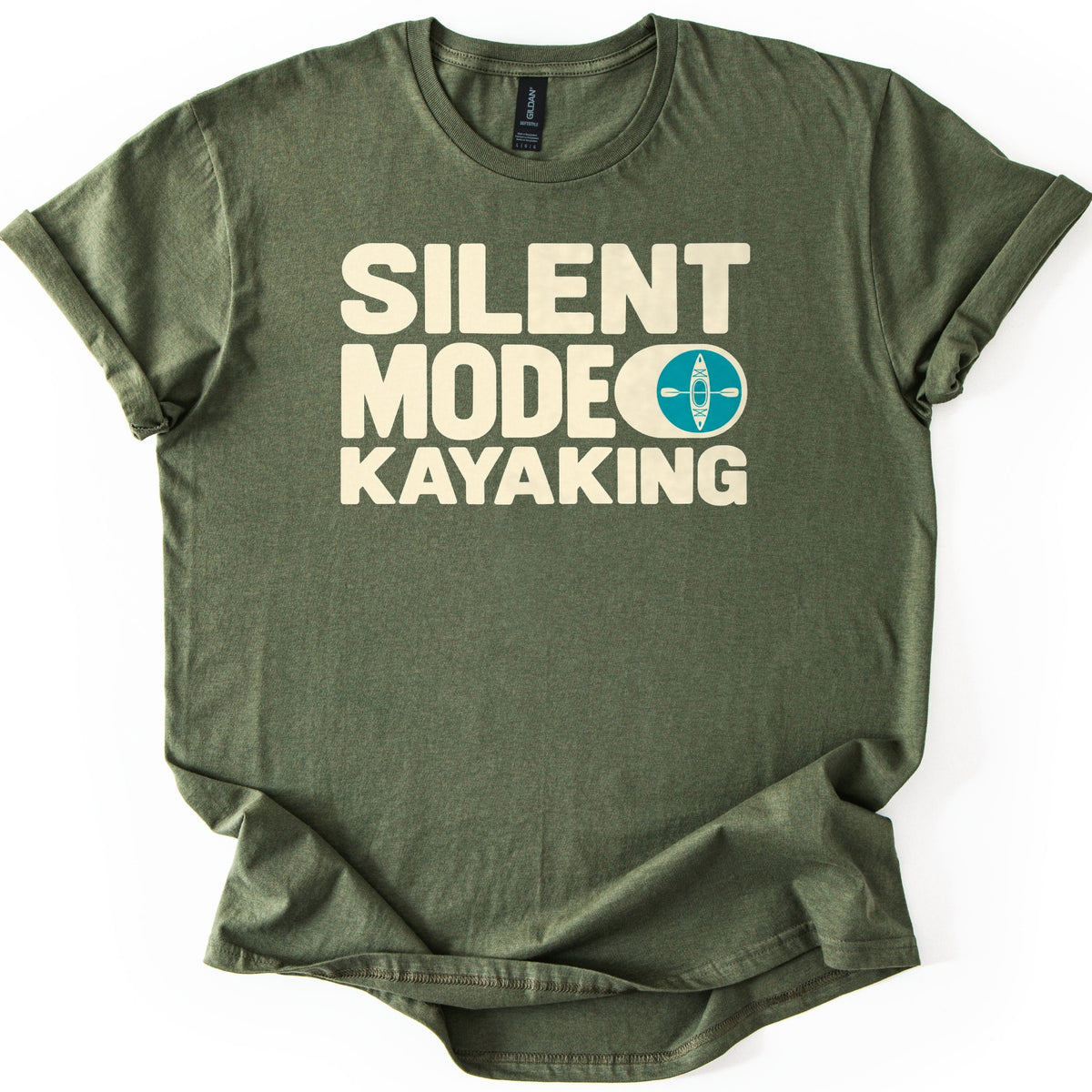Silent Mode Comfort Colors T-shirt in Military Green, laid flat. Bold cream block letters read Silent Mode Kayaking, with a teal circle showing a kayak and paddle from above beside the word Mode. The shirt has rolled sleeves on a white background.