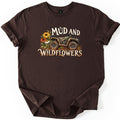 Mud and Wildflowers Comfort Colors T-shirt in Dark Chocolate, laid flat. A mud-splattered green ATV sits beside yellow, orange and white wildflowers between the words Mud and Wildflowers in cream lettering. The shirt has rolled sleeves on a white background.