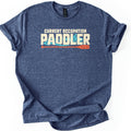Current Occupation Paddler Comfort Colors T-shirt in Heather Navy, laid flat. The words Current Occupation above a large Paddler in cream letters over swirling turquoise water, with an orange canoe paddle underneath. The shirt has rolled sleeves and lies on a white background.