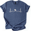Snow Boarder Pulse II Comfort Colors T-shirt in Heather Navy, laid flat. A cream heartbeat line runs across the chest, with a snowboarder silhouette riding a dip in the line; there are no words. The shirt lies on a white surface with its sleeves rolled.