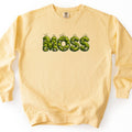 Moss Comfort Colors crewneck sweatshirt in Butter, laid flat. The word MOSS is printed across the chest in large letters made of green moss and gray stones, with small sprouts on top. The sweatshirt lies on a white background.