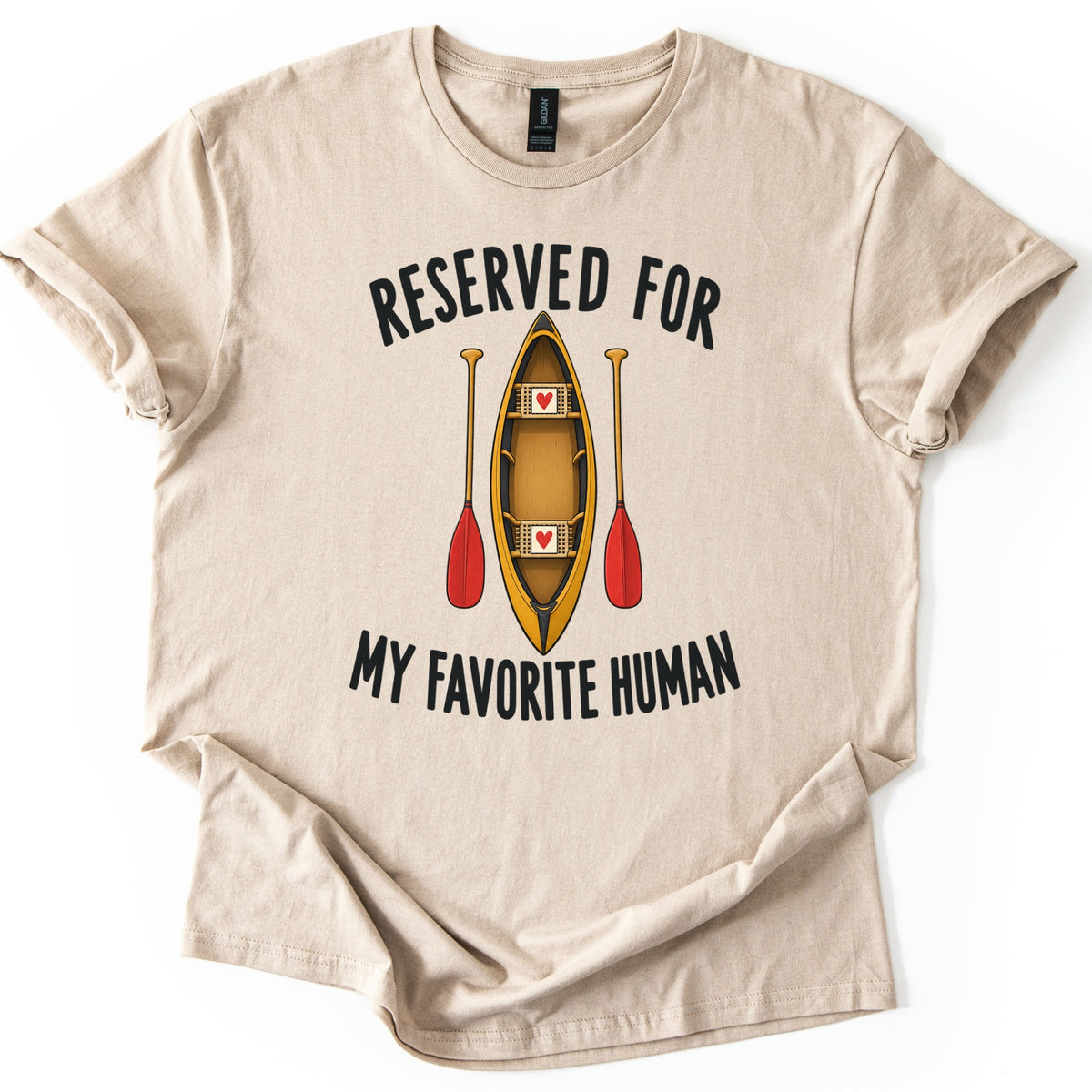 Reserved For My Favorite Human Comfort Colors T-shirt in Sand, laid flat. A yellow canoe seen from above, with a red heart on each of its two seats, sits between two red paddles under the words Reserved For and above My Favorite Human. Cuffed sleeves on a white background.