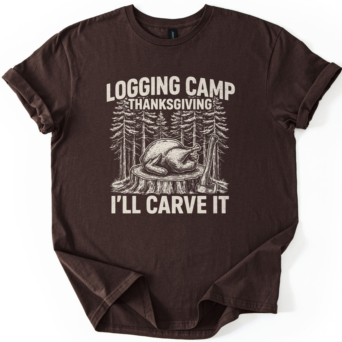 Logging Camp Thanksgiving Comfort Colors T-shirt in Dark Chocolate, laid flat. A cream-colored sketch of a roast turkey on a tree stump in a pine forest, with an axe leaning beside it, between the words Logging Camp Thanksgiving and I'll Carve It. Sleeves are cuffed on a white surface.
