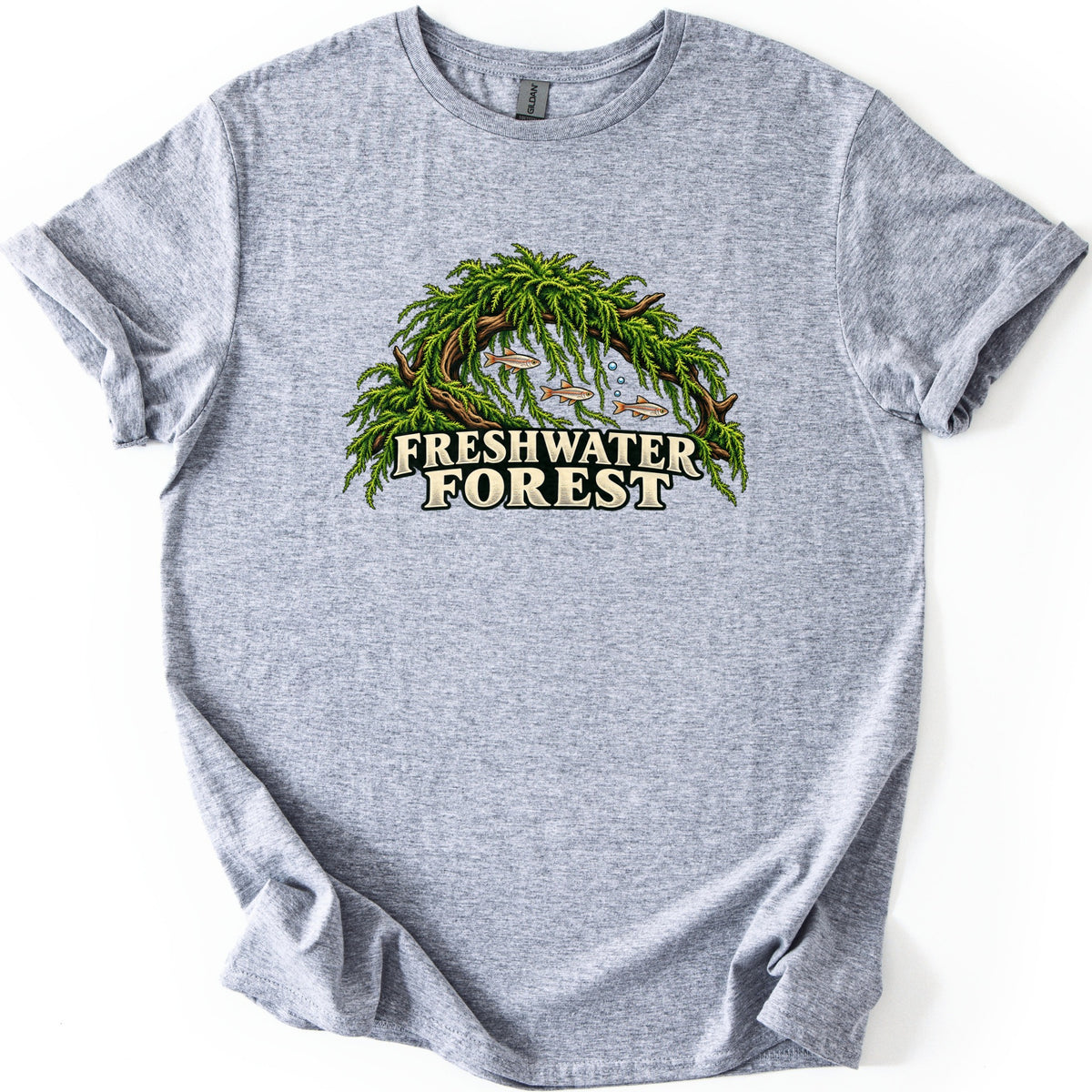 Freshwater Forest Comfort Colors T-shirt in Sport Grey, laid flat. An arch of driftwood draped in bright green aquarium moss shelters three small fish and rising bubbles, above the words Freshwater Forest in cream lettering. The sleeves are rolled on a white background.