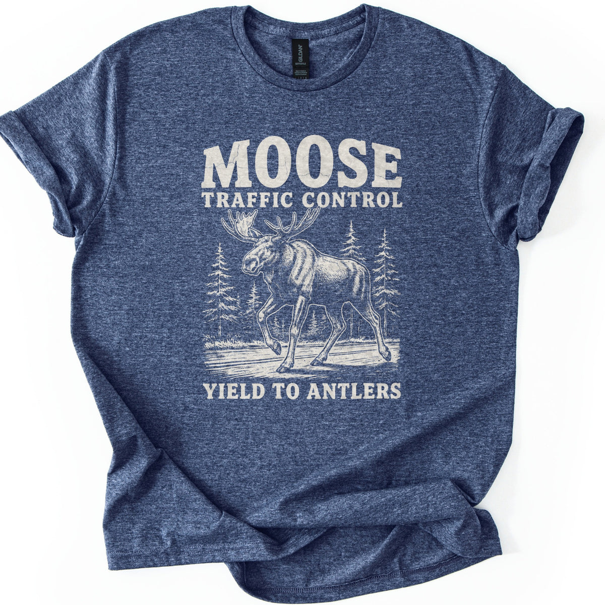 Moose Traffic Control Comfort Colors T-shirt in Heather Navy, laid flat. A cream sketch of a bull moose walking across a road between pine trees, under the words Moose Traffic Control and above Yield to Antlers. The sleeves are cuffed, on a plain white background.