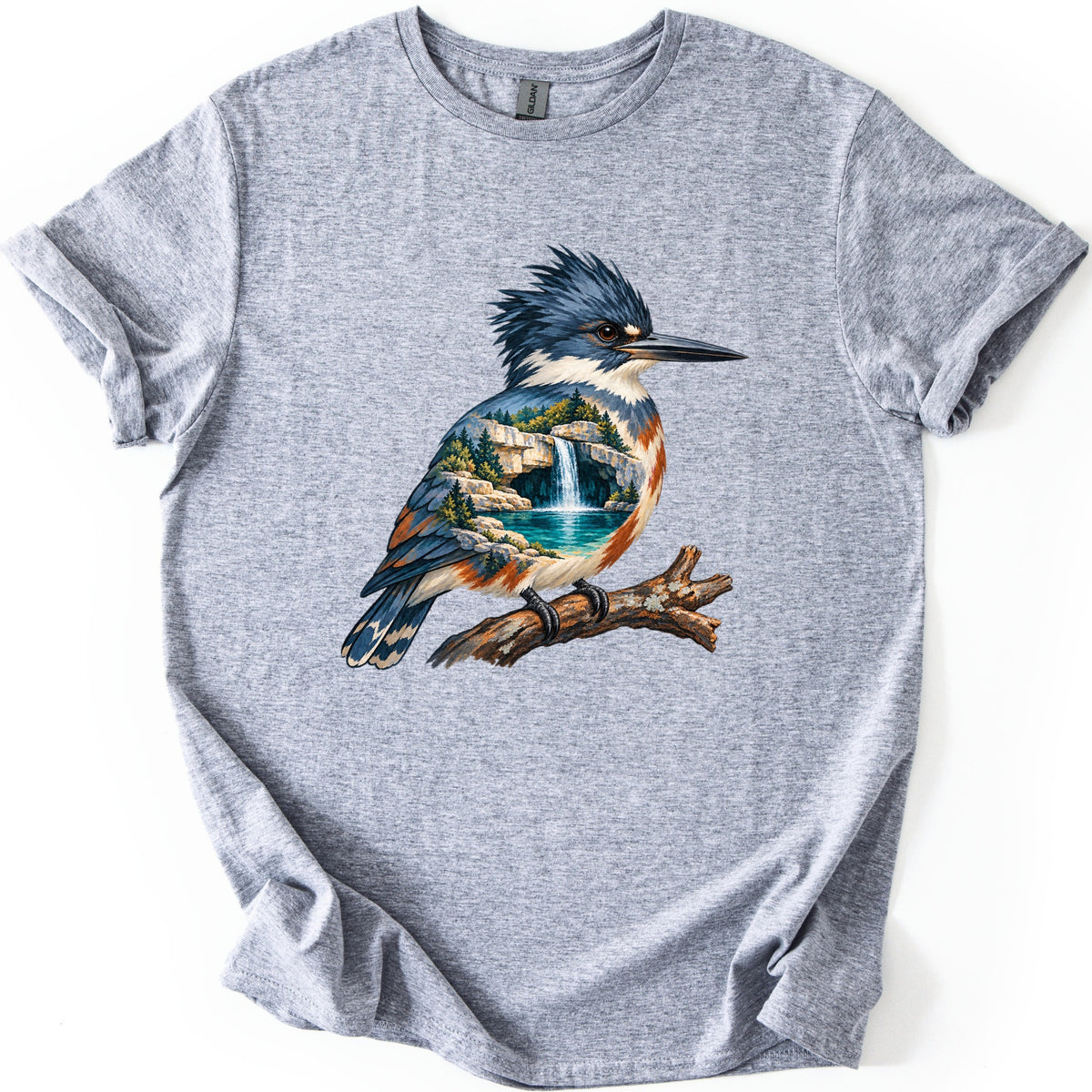 Kingfisher Waterfall Comfort Colors T-shirt in Sport Grey, laid flat. A painted kingfisher with a blue crest perches on a branch, its body filled with a waterfall pouring into a turquoise pool among rocks and pine trees. No words. Sleeves rolled, on a white background.