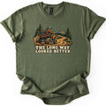 The Long Way Looked Better Comfort Colors T-shirt in Military Green, laid flat. A rider in an orange jacket and white helmet drives a red ATV along a winding dirt trail through pine trees toward mountains, above the words The Long Way Looked Better. The shirt lies on a white background.