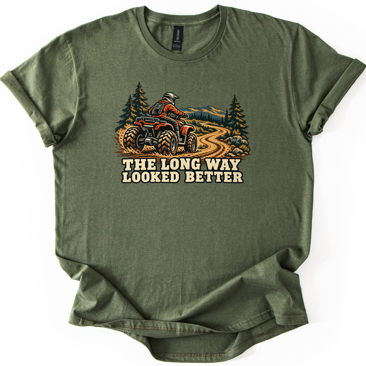 The Long Way Looked Better Comfort Colors T-shirt in Military Green, laid flat. A rider in an orange jacket and white helmet drives a red ATV along a winding dirt trail through pine trees toward mountains, above the words The Long Way Looked Better. The shirt lies on a white background.