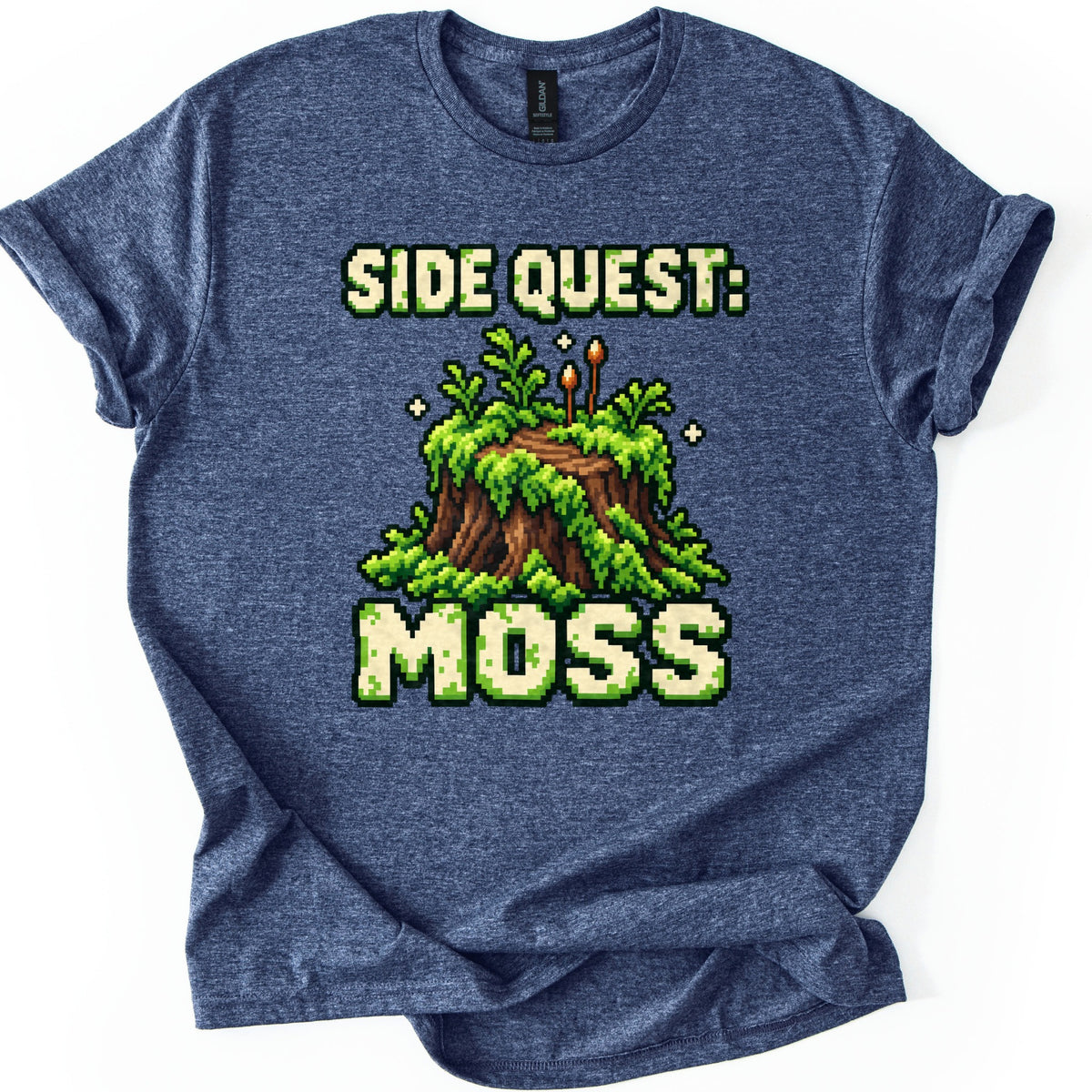 Side Quest Moss Comfort Colors T-shirt in Heather Navy, laid flat. A pixel-art tree stump covered in green moss and ferns, with two tiny spore stalks and sparkles, sits between the words Side Quest: and Moss in cream pixel letters. White background, rolled sleeves.