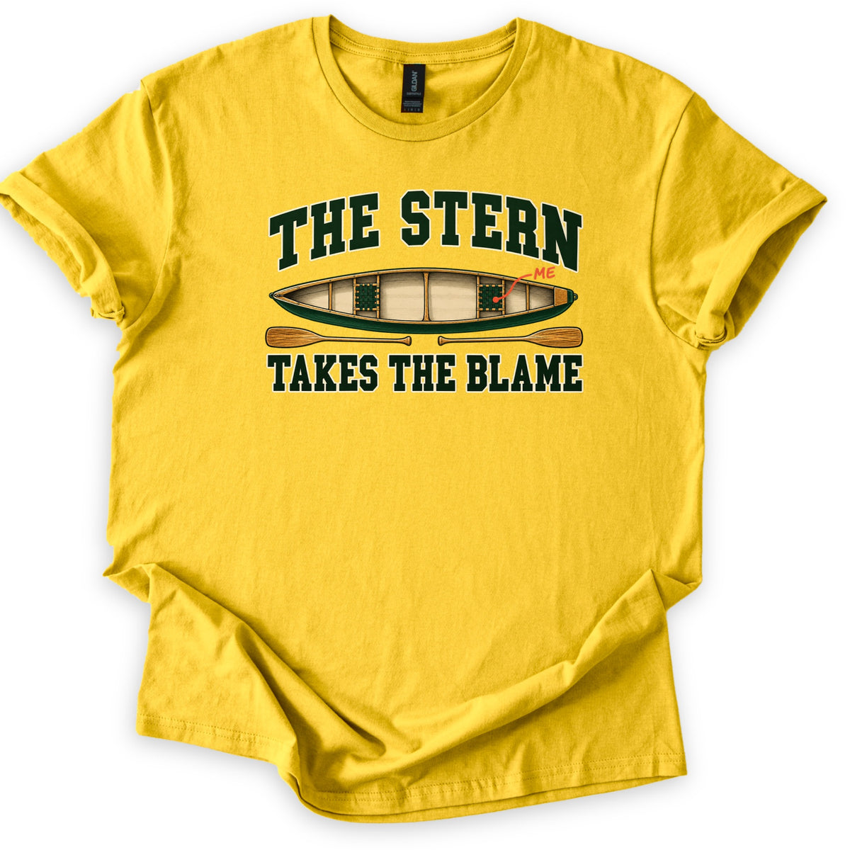 The Stern Takes the Blame Comfort Colors T-shirt in Daisy, laid flat. The words The Stern above a green wooden canoe seen from above, with a red line marking the back seat labeled Me, two crossed paddles below, and the words Takes the Blame. Sleeves rolled, on a white background.