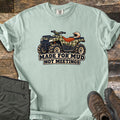 Made for Mud Not Meetings Comfort Colors T-shirt in Bay, laid flat. A green plaid ATV with an orange seat, muddy tires and a white helmet on the rack sits above the words Made for Mud Not Meetings. It lies on weathered wood beside folded olive pants and brown hiking boots.