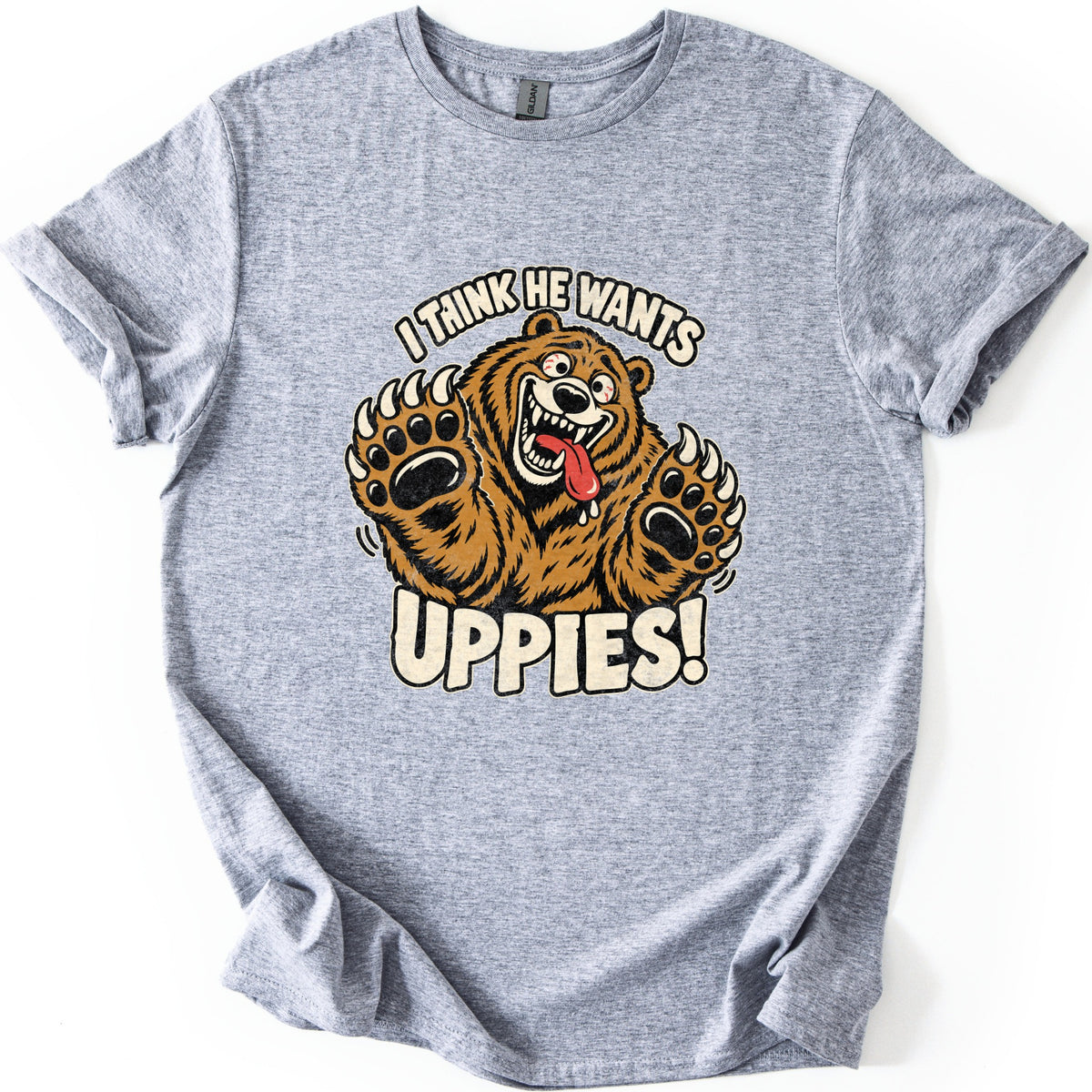 I Think He Wants Uppies Comfort Colors T-shirt in Sport Grey, laid flat. A wild-eyed cartoon brown bear grins with its tongue hanging out and raises both clawed paws between the words I Think He Wants and Uppies! The sleeves are cuffed on a white background.