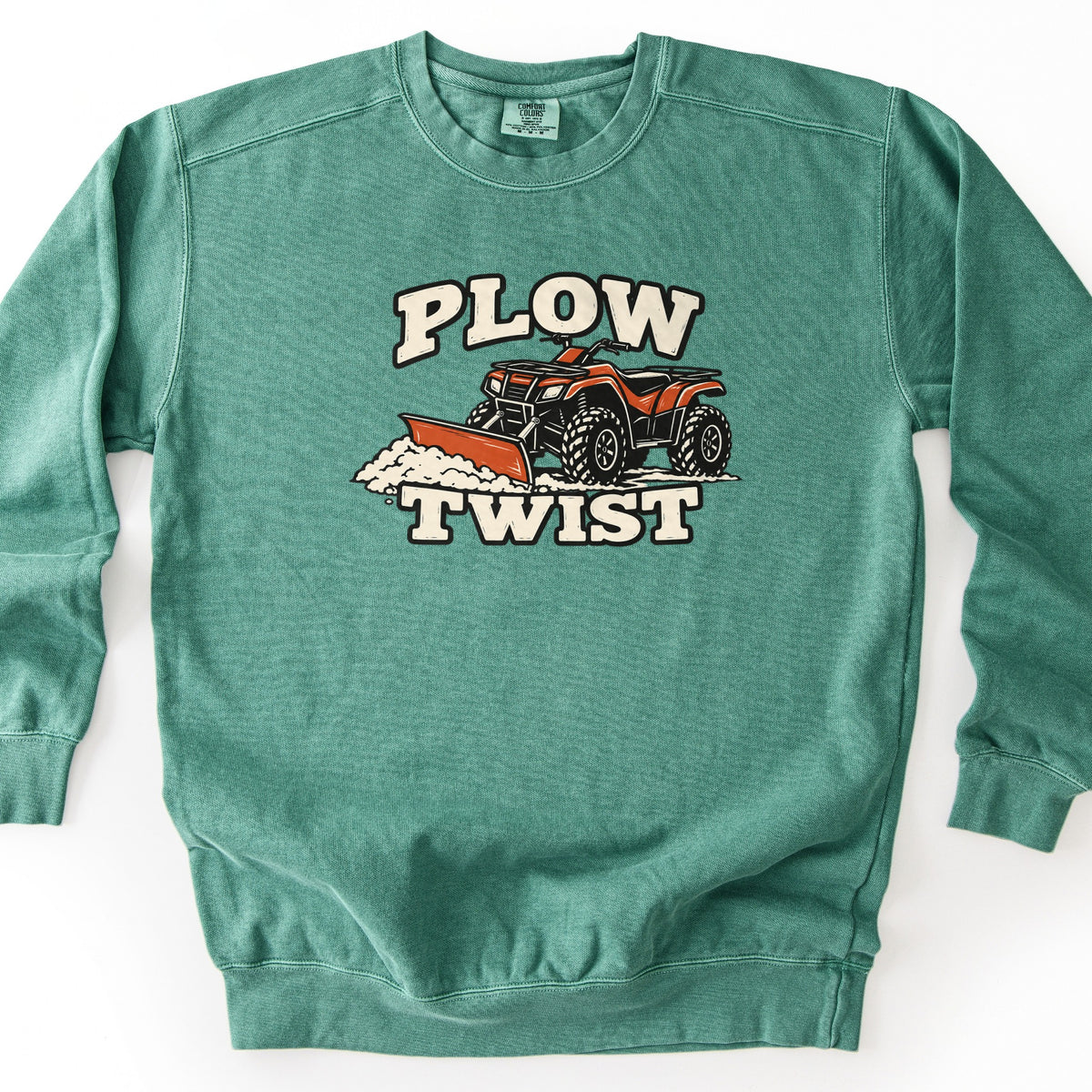 Plow Twist Comfort Colors crewneck sweatshirt in Light Green, laid flat. The words Plow Twist in cream block letters frame an illustration of a red ATV with a front plow blade pushing snow. The sweatshirt lies on a white surface.