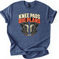 Knee Pads Big Plans Comfort Colors T-shirt in Heather Navy, laid flat. The words Knee Pads Big Plans in cream and orange-red block letters arch above a pair of black and cream knee pads, with MTB between orange bars below. The shirt has rolled sleeves on a white background.