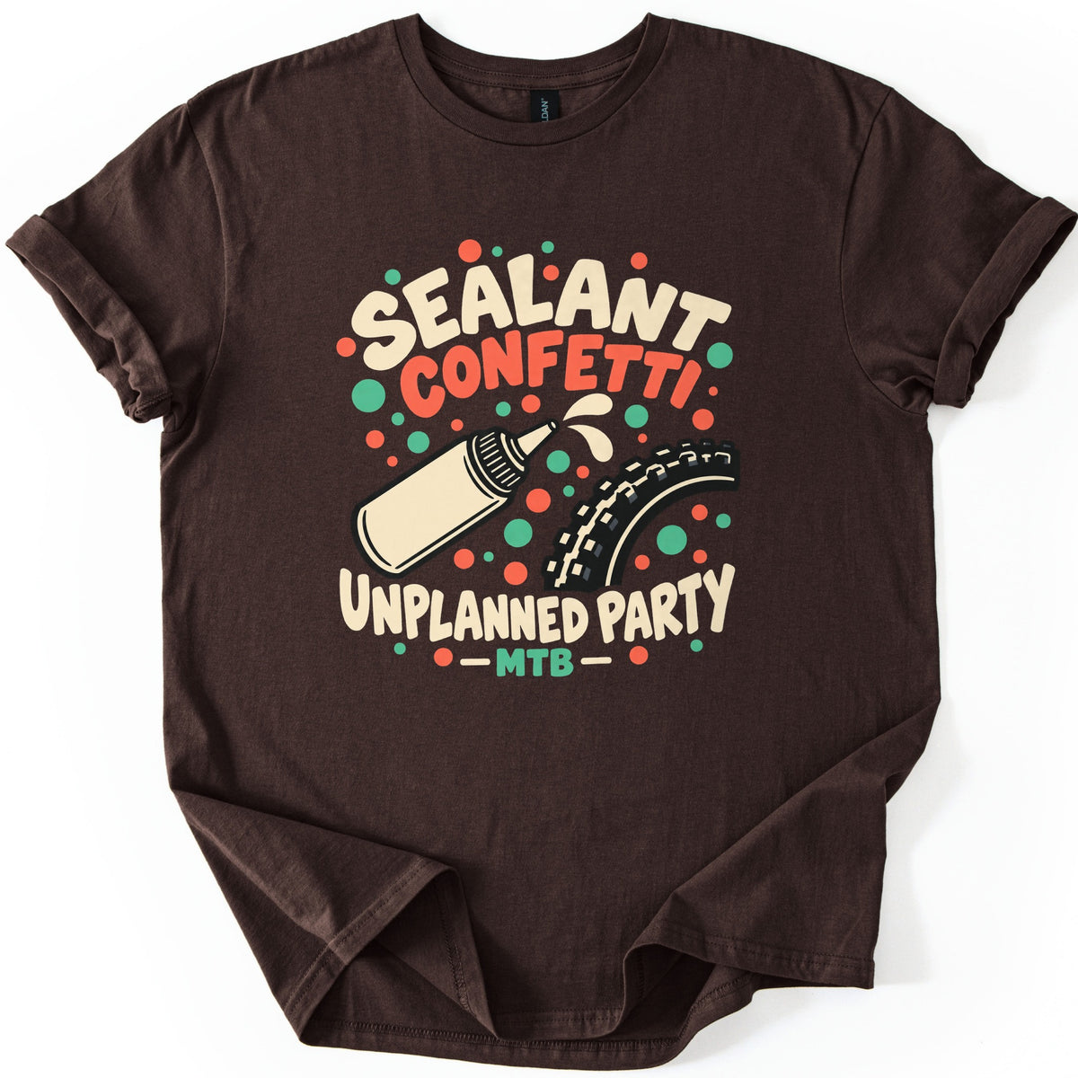 Sealant Confetti Unplanned Party Comfort Colors T-shirt in Dark Chocolate, laid flat. A cream squeeze bottle squirts sealant at a knobby bike tire amid red and green confetti dots, with the words Sealant Confetti, Unplanned Party, MTB. Sleeves are rolled, on a white background.