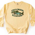Cold Water Clear Mind Comfort Colors crewneck sweatshirt in Butter, laid flat. A spotted trout with a pine forest, rocks and a turquoise river inside its body, between the dark green words Cold Water arched above and Clear Mind below. Shown on a white background.