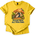 Please Wipe All Four Paws Comfort Colors T-shirt in Daisy, laid flat. A hedgehog stands on a woven doormat outside a mushroom cottage with an orange spotted cap and blue door, framed by ferns and berries. Below, dark green text reads Please Wipe All Four Paws.