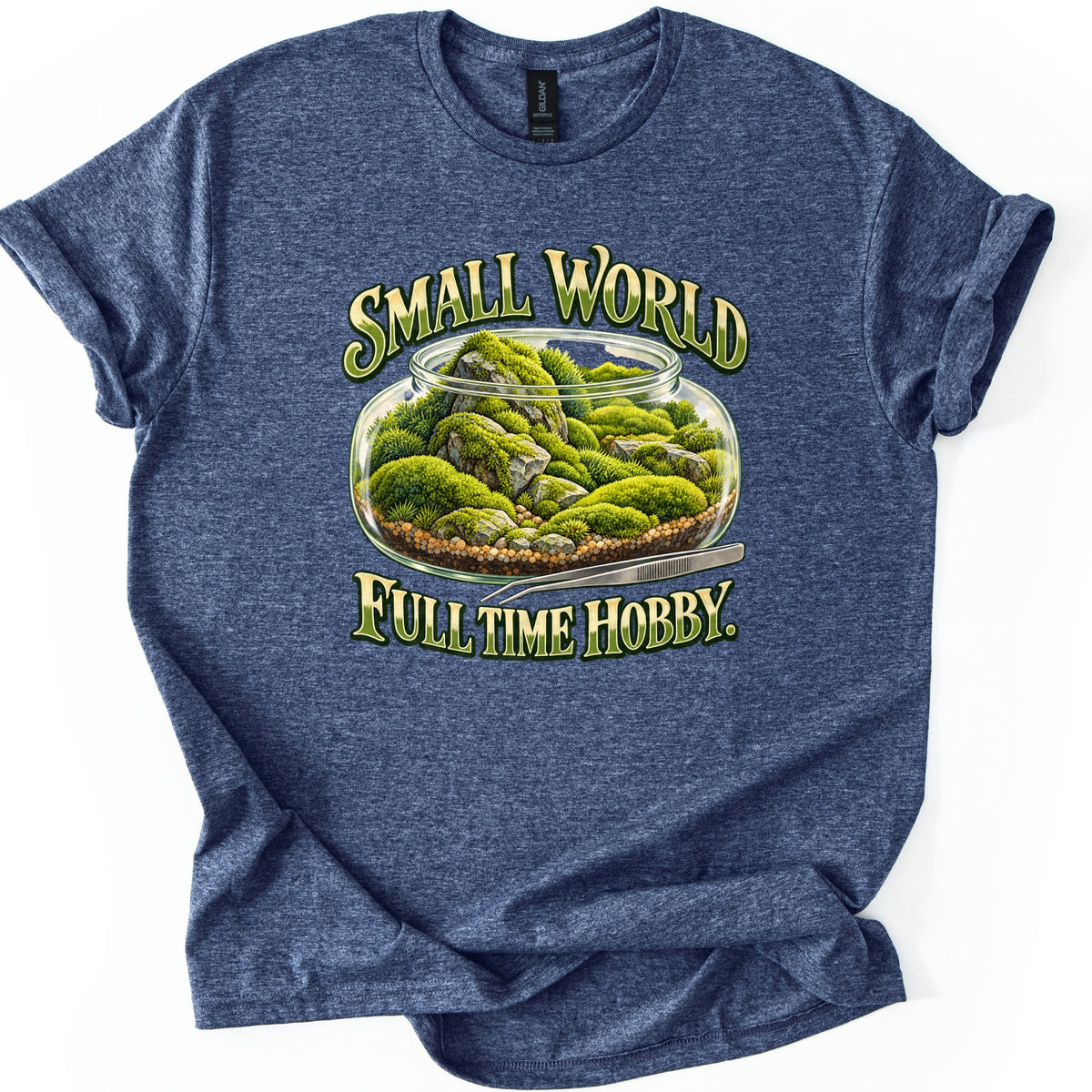 Small World Full Time Hobby Comfort Colors T-shirt in Heather Navy, laid flat. A glass terrarium jar of green moss and gray rocks on gravel, with metal tweezers beside it, between the words Small World and Full Time Hobby. in green and gold letters. Sleeves cuffed, on a white background.