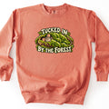 Tucked in by the Forest Comfort Colors crewneck sweatshirt in Terracotta, laid flat. A sleeping gray mouse lies on a log under a blanket of green moss, framed by the words Tucked In By the Forest in cream lettering. The sweatshirt lies on a white background.