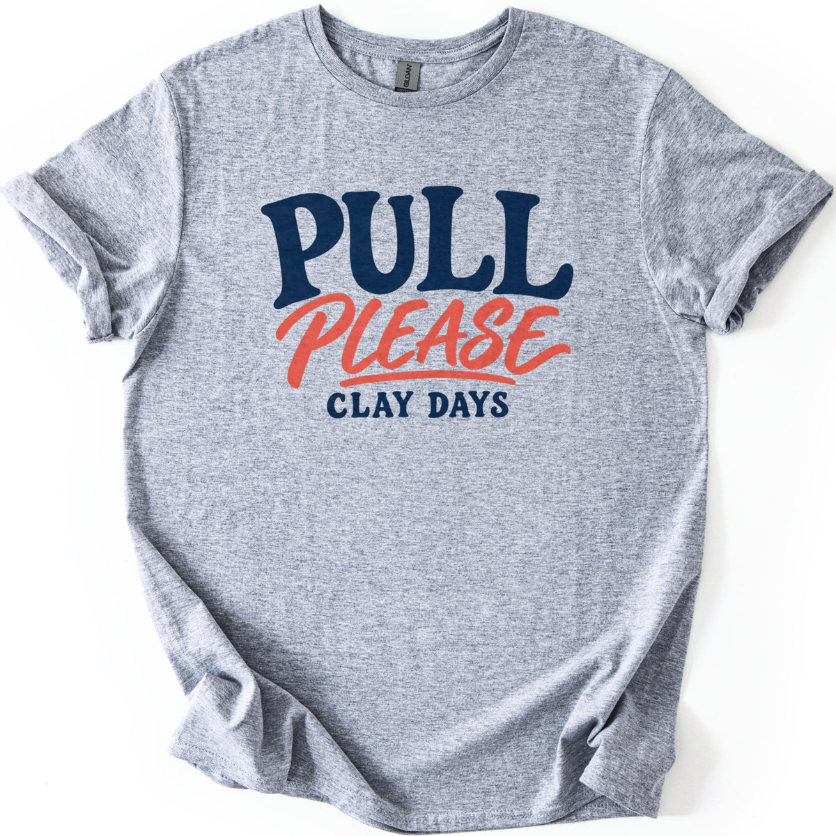 Pull Please Comfort Colors T-shirt in Sport Grey, laid flat. Bold navy letters read PULL above the word PLEASE in coral script with an underline swash, and smaller navy letters below read CLAY DAYS. The sleeves are rolled and the shirt lies on a white background.