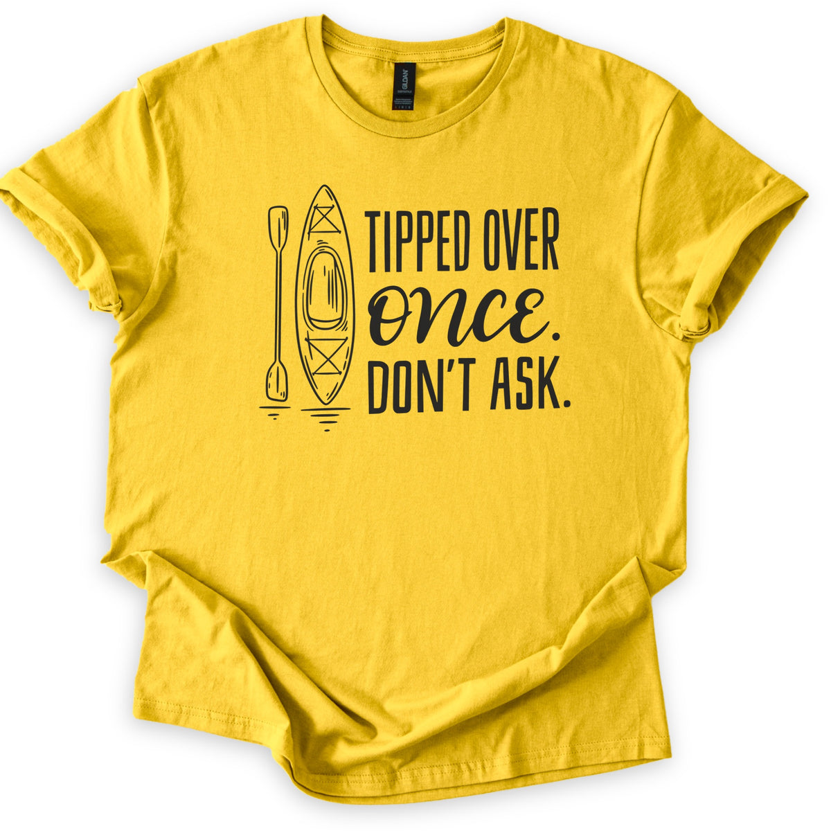 Tipped Over Once Kayak Comfort Colors T-shirt in Daisy, laid flat. A black line drawing of an upright kayak and paddle with water ripples sits beside the words Tipped Over Once. Don't Ask., with Once in script. The shirt has cuffed sleeves on a white background.