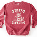 Stress Cleaning Comfort Colors crewneck sweatshirt in Crimson, laid flat. Cream print of a sketched raccoon standing in rippling water, washing an apple, between the words STRESS and CLEANING. The sweatshirt lies on a white surface.