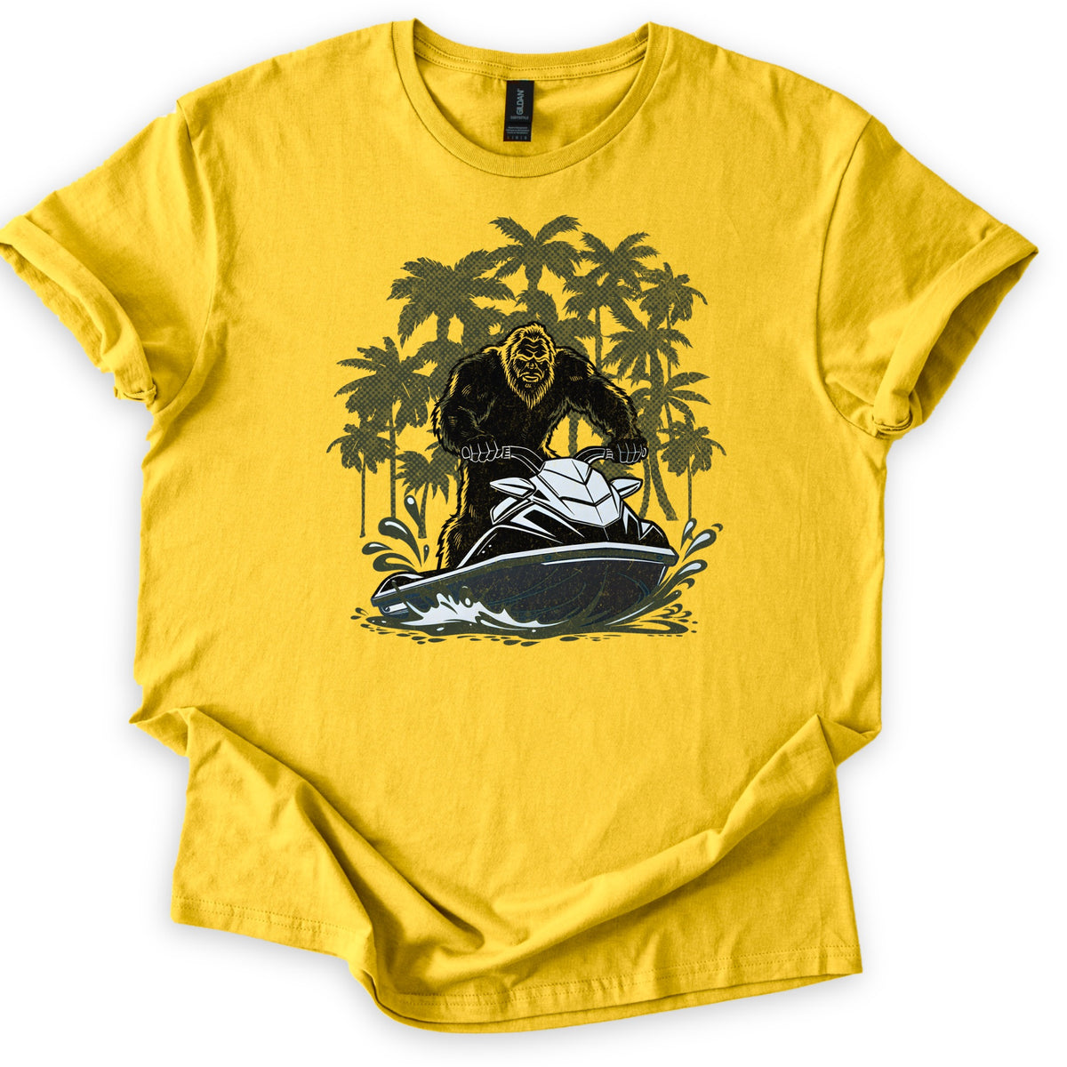 Jet Ski Squatch Comfort Colors T-shirt in Daisy, laid flat. A black-furred Bigfoot rides a black and white jet ski through splashing water, with olive green palm trees behind him. No words are printed. The shirt lies on a white background with rolled sleeves.