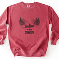 My Kind Of Commute Comfort Colors crewneck sweatshirt in Crimson, laid flat. A black sketch-style drawing of a man paddling a canoe across a calm lake between misty pine-covered shores, above the words My Kind Of Commute. The sweatshirt lies on a plain white surface.