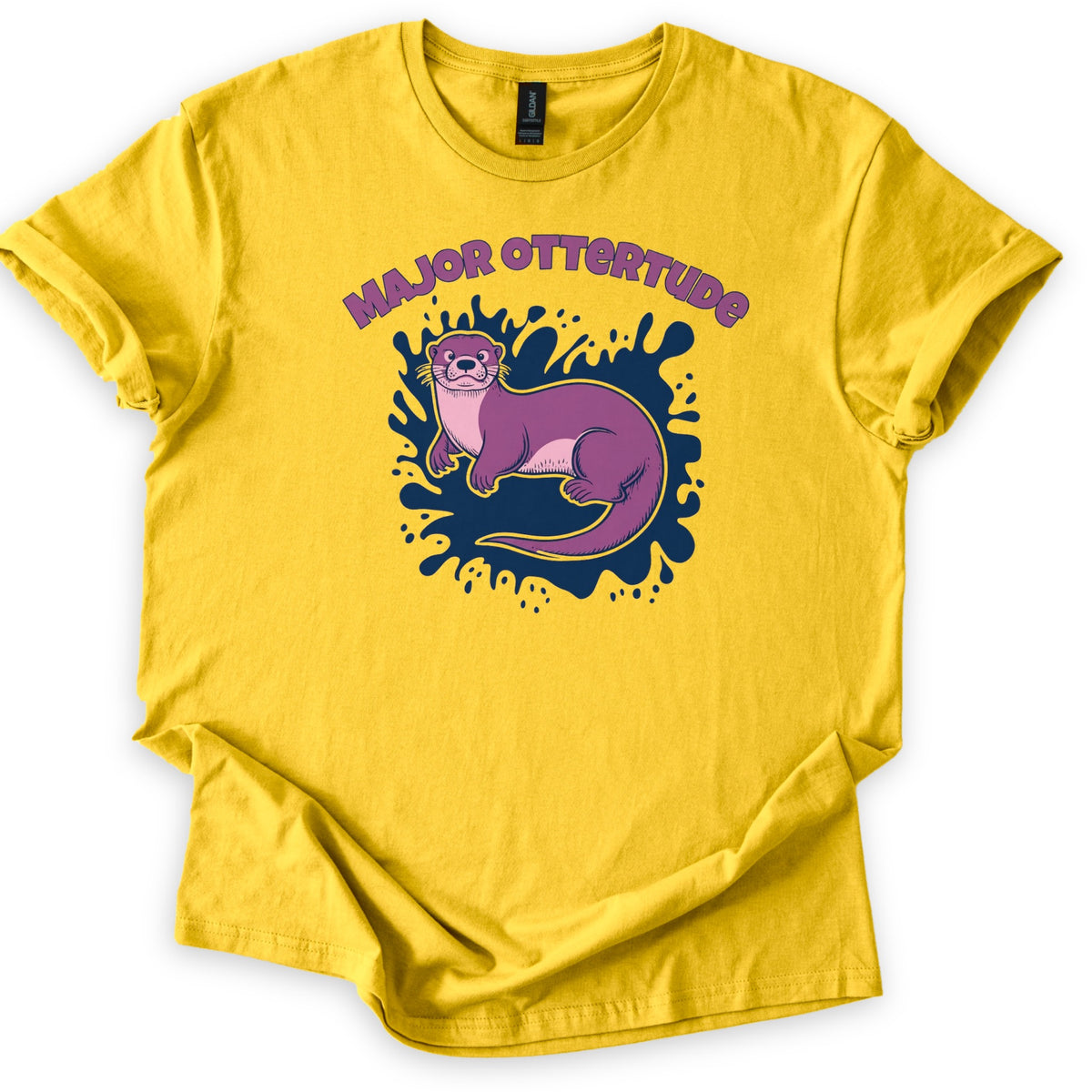 Major Ottertude Comfort Colors T-shirt in Daisy, laid flat. A purple cartoon otter with a pink chest lies on a navy blue paint splash under arched purple letters reading MAJOR OTTERTUDE. The shirt has cuffed sleeves and lies on a white background.