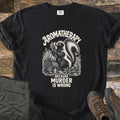 Aromatherapy Because Murder Is Wrong Comfort Colors T-shirt in Black, laid flat. An engraving-style skunk sniffs a bundle of lavender among flowers, a basket and an oil bottle, in cream ink, with the words Aromatherapy, Because Murder Is Wrong. Olive pants and brown hiking boots lie on wood planks.
