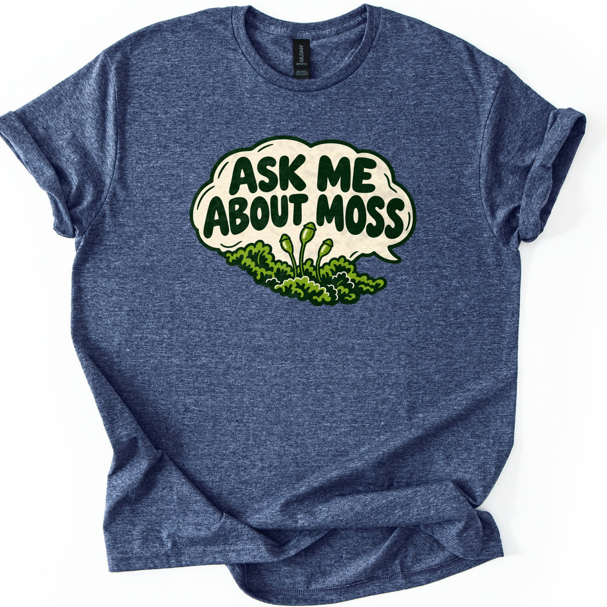 Ask Me About Moss Comfort Colors T-shirt in Heather Navy, laid flat. A cream speech bubble reads ASK ME ABOUT MOSS in bold dark green letters above a cartoon clump of green moss with three stalked spore capsules. The shirt has rolled sleeves on a white background.