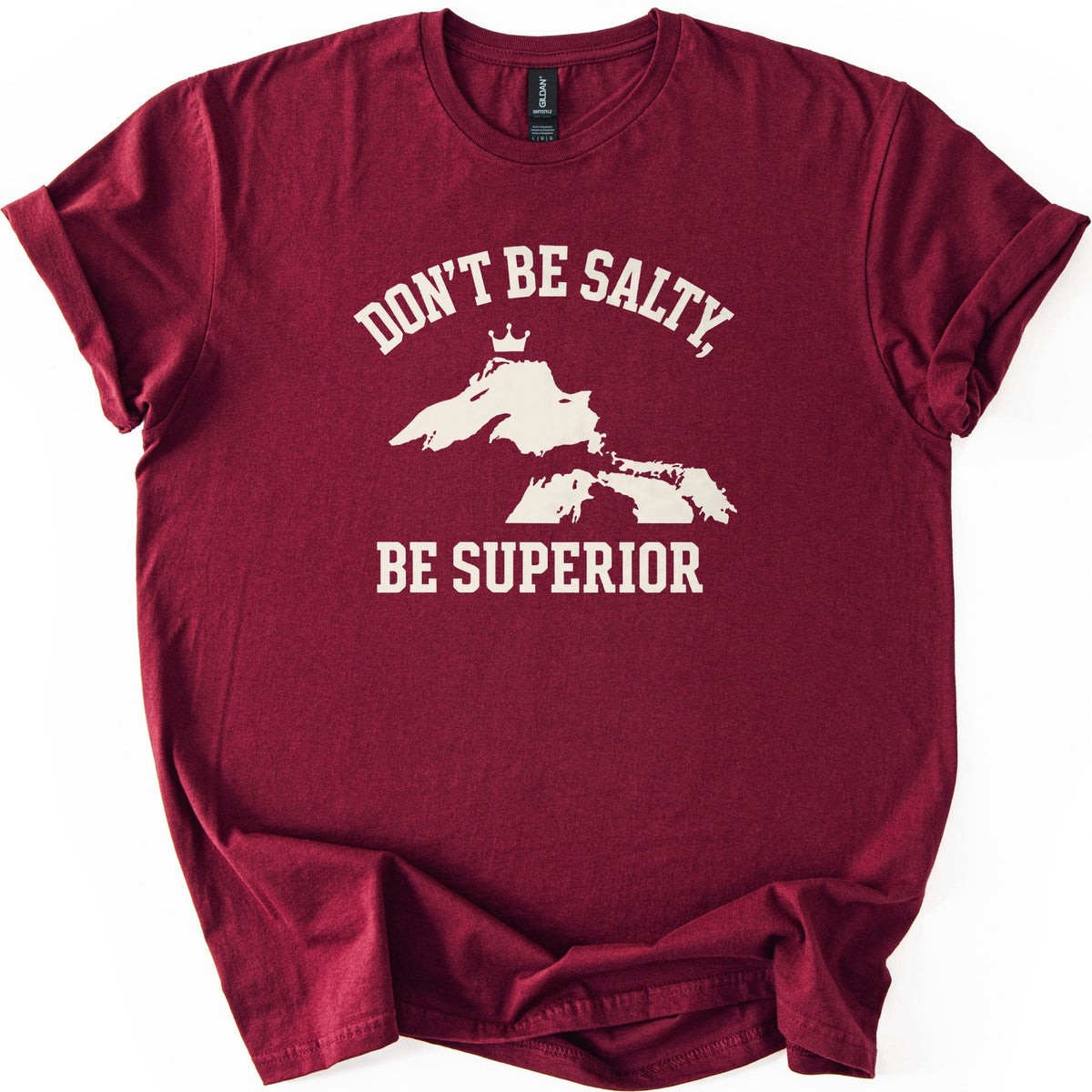 Be Superior Comfort Colors T-shirt in Maroon, laid flat. A cream print shows the words Don't Be Salty, arched over a silhouette of the Great Lakes with a small crown above Lake Superior, and Be Superior below. Sleeves are cuffed on a white background.