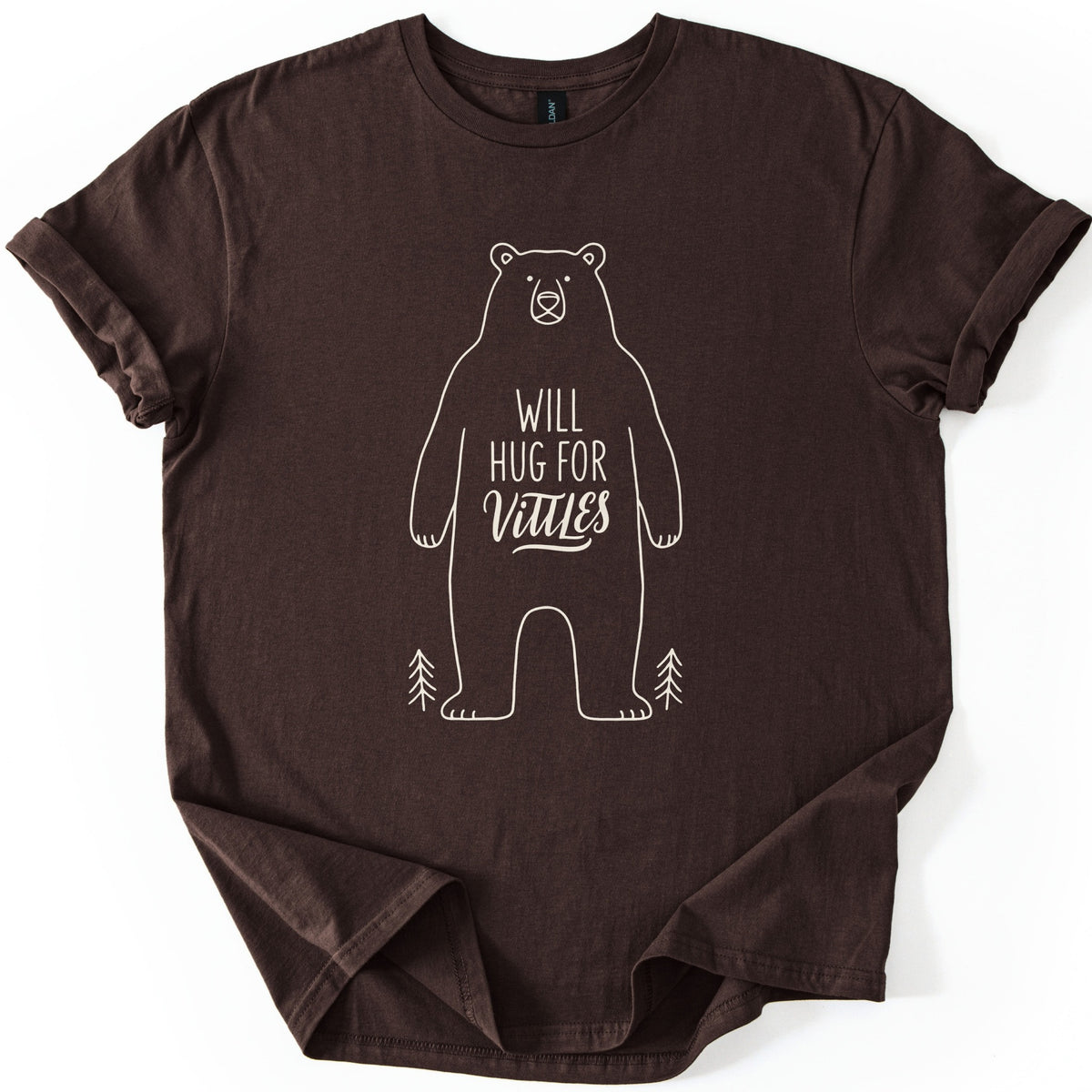Will Hug For Vittles Bear Comfort Colors T-shirt in Dark Chocolate, laid flat. A cream line drawing of a standing bear with the words WILL HUG FOR Vittles on its belly and a small pine tree at each foot. The shirt has rolled sleeves and lies on a white background.