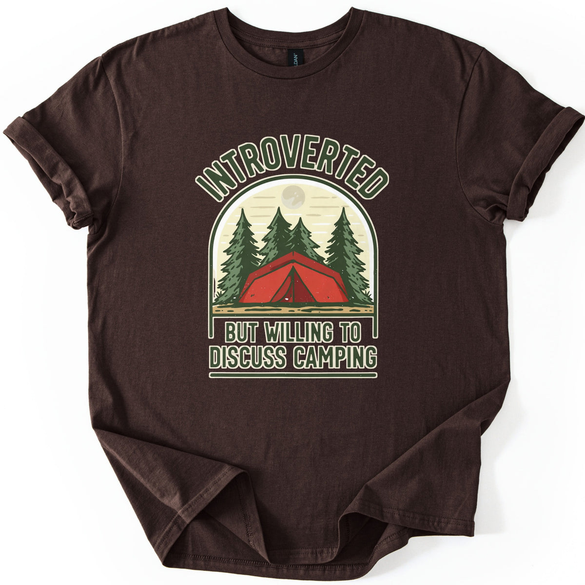 Introverted Camping Comfort Colors T-shirt in Dark Chocolate, laid flat. An arched badge shows a red tent among green pine trees under a pale moon, with INTROVERTED curved above and BUT WILLING TO DISCUSS CAMPING below. The shirt lies on a white background with rolled sleeves.