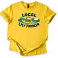 Lily Paddler Comfort Colors T-shirt in Daisy, laid flat. A cartoon frog in an orange life vest paddles a green kayak past lily pads and a white water lily, between the words Local Lily Paddler in navy. The shirt has rolled sleeves on a white background.