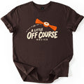 A Little Off Course Comfort Colors T-shirt in Dark Chocolate, laid flat. An orange two-winged helice target with a cream center flies along a dashed arc above cream lettering reading A Little Off Course, with Helice below. The shirt has rolled sleeves on a white background.