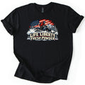 Life Liberty Fresh Powder Comfort Colors T-shirt in Black, laid flat. A rider in a red jacket and helmet kicks up snow on a snowmobile in front of an American flag, pine trees and a mountain, above the words Life Liberty Fresh Powder. Sleeves rolled, on a white background.
