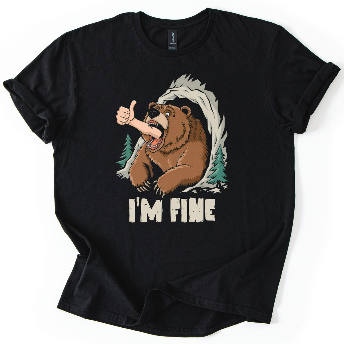 Grizzly I'm Fine Comfort Colors T-shirt in Black, laid flat. A cartoon grizzly bear bursts from a rocky cave between pine trees, a human arm giving a thumbs up sticking out of its open jaws, above the words I'M FINE. The shirt has rolled sleeves on a white surface.