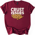 Crust Issues Comfort Colors T-shirt in Maroon, laid flat. Cream block letters read CRUST ISSUES above a cartoon lattice-top pie with a wooden rolling pin. The shirt has rolled sleeves and lies on a plain white background.