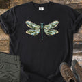 Braided River Dragonfly Comfort Colors T-shirt in Black, laid flat. A dragonfly with a teal body and wings filled with braided rivers, forests and mountains is printed on the chest, with no words. Olive cargo pants and brown hiking boots lie beside it on weathered wood.