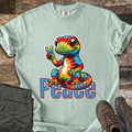 Peace Comfort Colors T-shirt in Bay, laid flat. A smiling rainbow tie-dye gecko sits flashing a peace sign above the word Peace in blue letters outlined in red. Shown on weathered wood with folded olive pants and brown hiking boots.