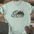 Cast and Cruise Comfort Colors T-shirt in Bay, laid flat. A trout leaps from splashing water beside an ATV with a fishing rod on rocks, above the words Cast and Cruise. Sleeves are rolled on a wood surface with olive cargo pants and brown hiking boots.