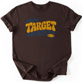 Very Target Oriented Comfort Colors T-shirt in Dark Chocolate, laid flat. The word Very in blue script sits above Target in bold mustard-yellow bubble letters and Oriented in blue, with a swoosh leading to a yellow clay pigeon. The shirt has rolled sleeves on a white background.