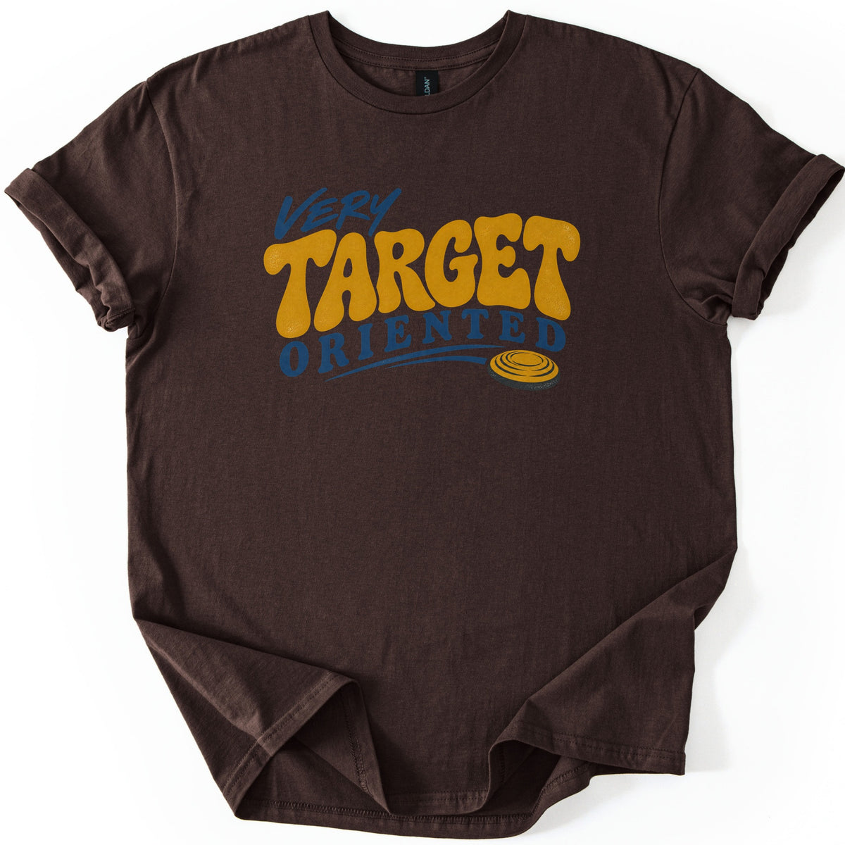 Very Target Oriented Comfort Colors T-shirt in Dark Chocolate, laid flat. The word Very in blue script sits above Target in bold mustard-yellow bubble letters and Oriented in blue, with a swoosh leading to a yellow clay pigeon. The shirt has rolled sleeves on a white background.