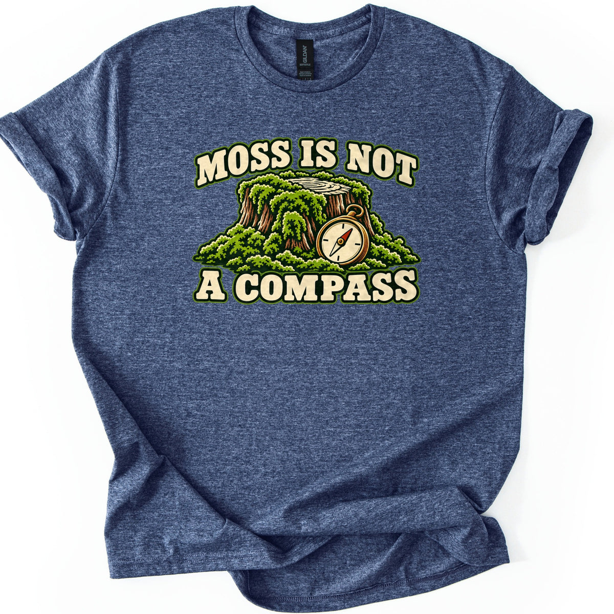 Moss Is Not a Compass Comfort Colors T-shirt in Heather Navy, laid flat. The words Moss Is Not arch above a moss-covered tree stump with a brass pocket compass leaning against it, with A Compass printed below. The shirt lies on a white background with cuffed sleeves.