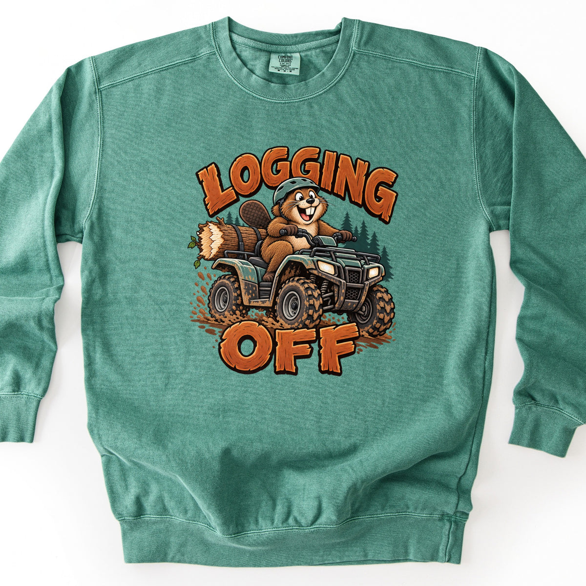 Logging Off Comfort Colors crewneck sweatshirt in Light Green, laid flat. A grinning cartoon beaver in a green helmet rides a muddy green ATV hauling a log past pine trees, between the words LOGGING OFF in orange wood-grain letters. The sweatshirt lies on a white surface.