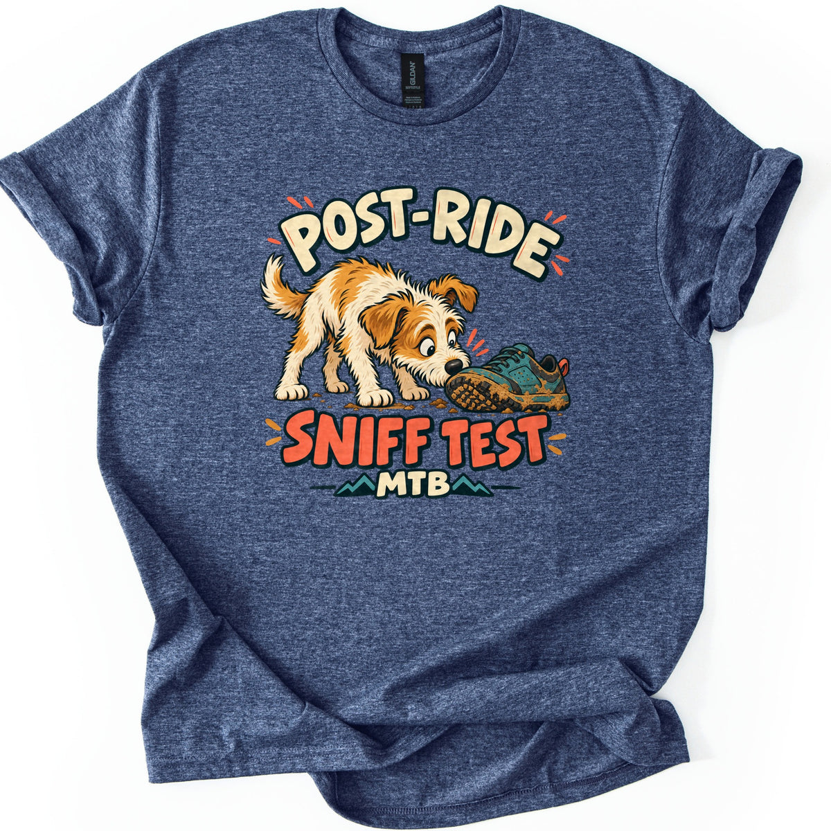 Post Ride Sniff Test Comfort Colors T-shirt in Heather Navy, laid flat. A scruffy tan and white cartoon dog sniffs a muddy teal sneaker between the words Post-Ride and Sniff Test, with MTB below over small mountain peaks. The shirt has rolled sleeves on a white background.