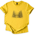 Snowy Log Cabin Comfort Colors T-shirt in Daisy, laid flat. A pencil-style sketch of a snow-covered log cabin with a smoking chimney and one window, set between snowy pine trees on a drift. No words. Sleeves are rolled on a white background.